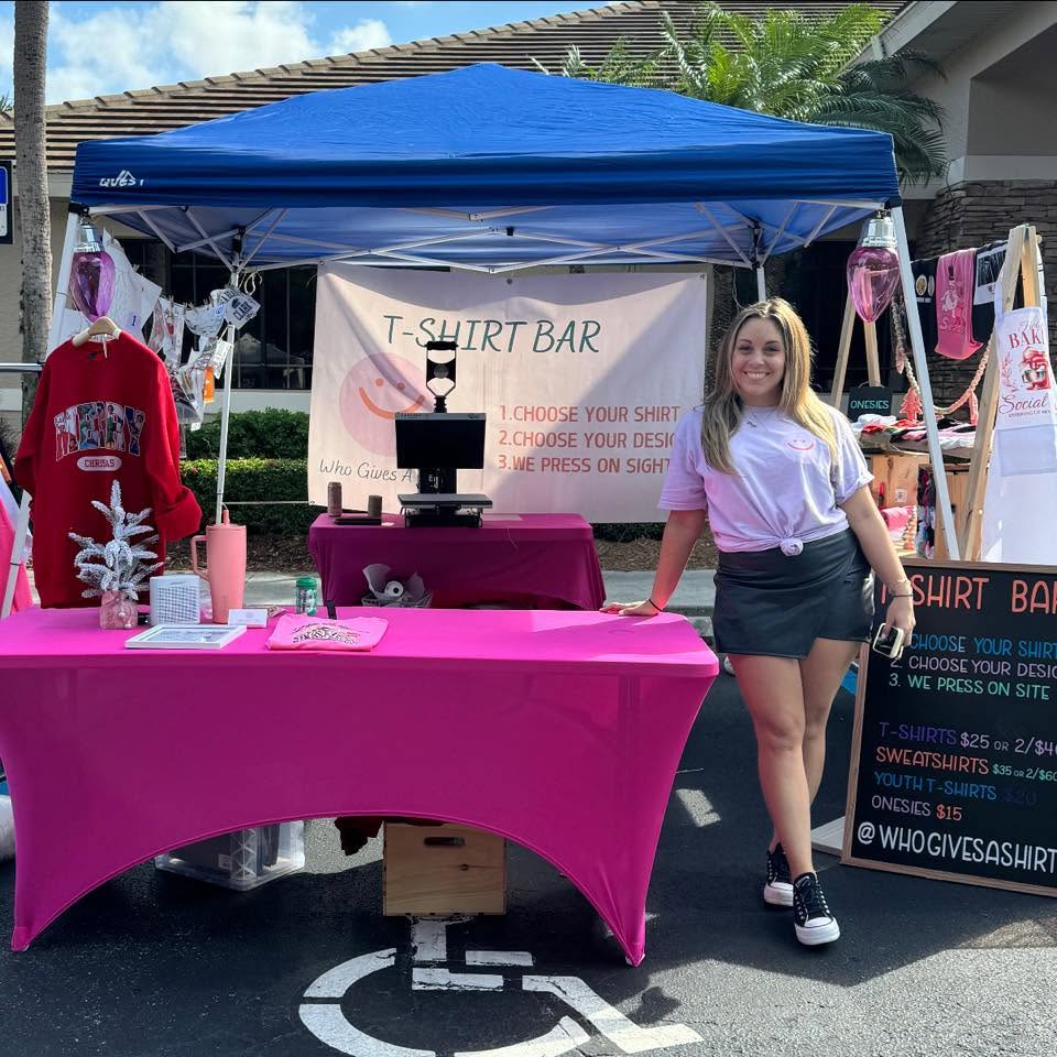 Who Gives A Shirt LLC pop-up T-Shirt Bar booth, with custom shirts on display and a heat press ready to go